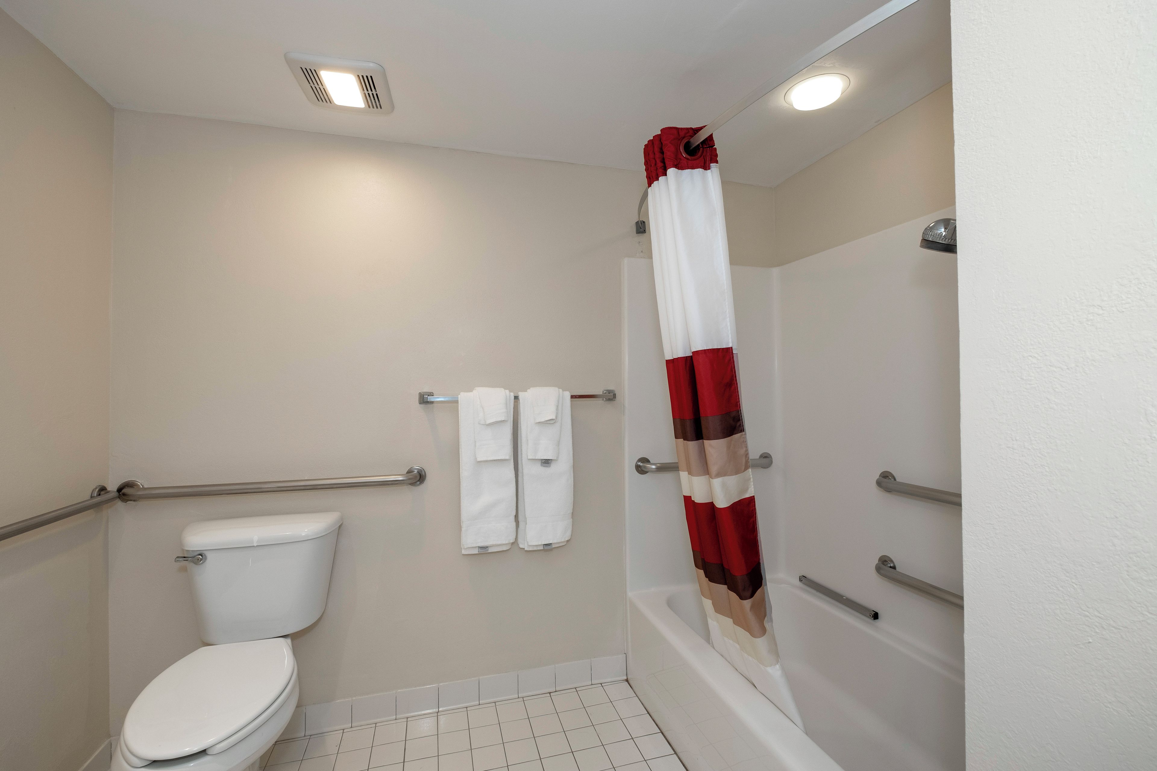 A bathroom with a toilet, a shower with a red and white curtain, and a grab bar.