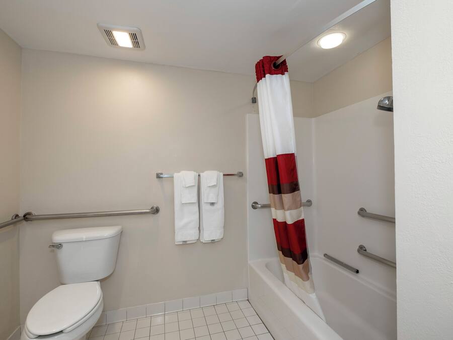A bathroom with a toilet, a shower with a red and white curtain, and a grab bar.