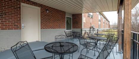 Un patio techado al aire libre con mesas y sillas de metal, un muro de ladrillo y una puerta.