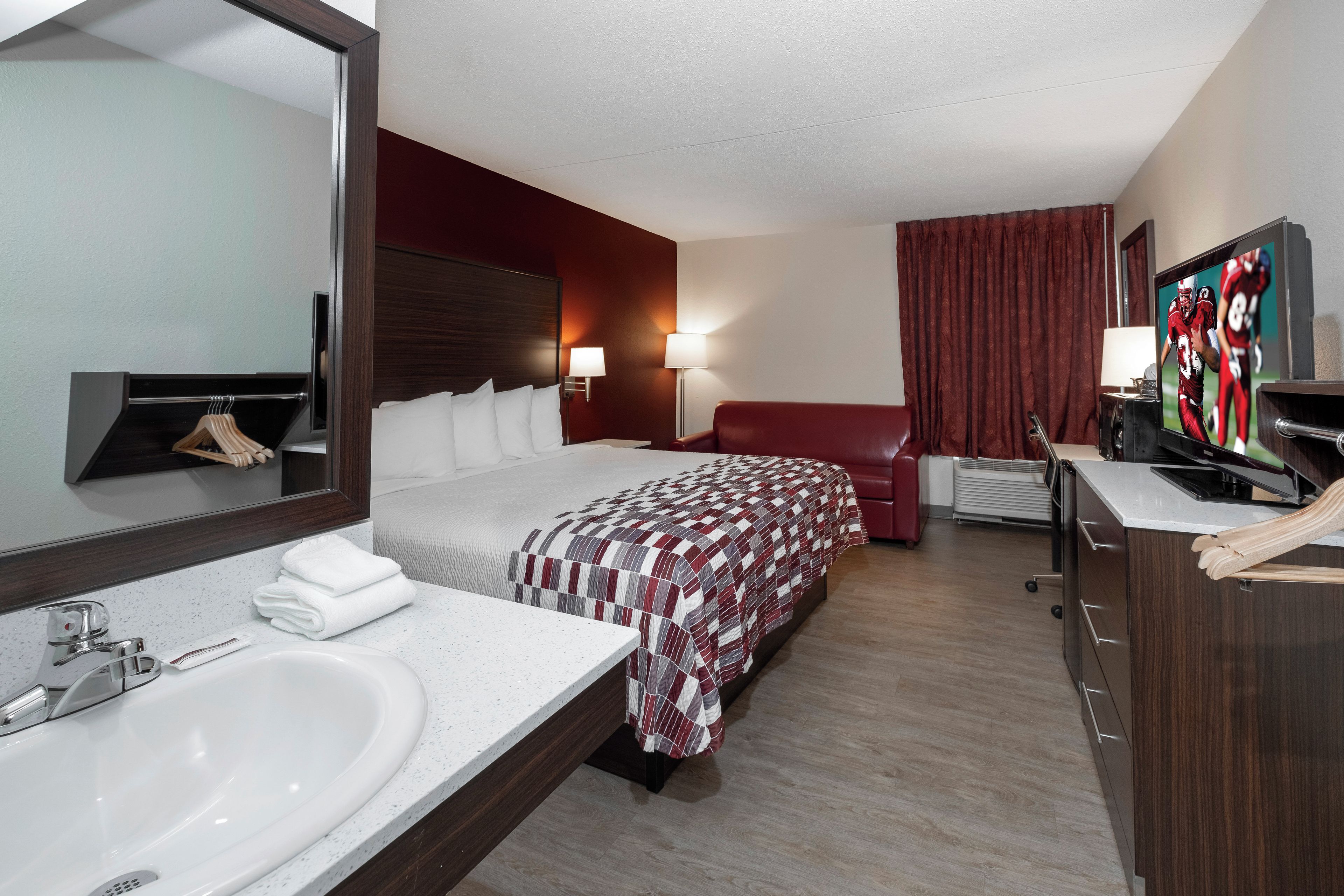 Een hotelkamer met een bed, een grote spiegel, een badkamer met een wastafel en een televisie.