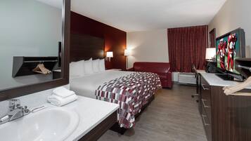 Een hotelkamer met een bed, een grote spiegel, een badkamer met een wastafel en een televisie.