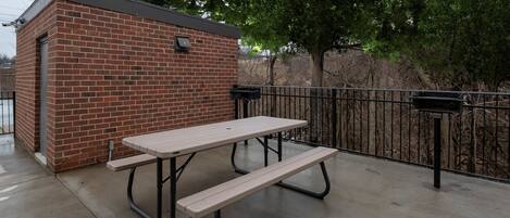 A picnic table with benches, a brick building, and a metal fence.