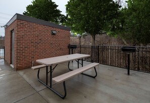 A picnic table with benches, a brick building, and a metal fence.