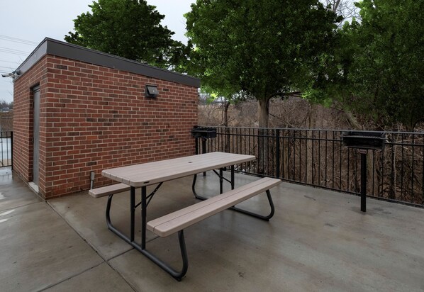 A picnic table with benches, a brick building, and a metal fence. - Red Roof Inn Leesburg, VA (Leesburg)