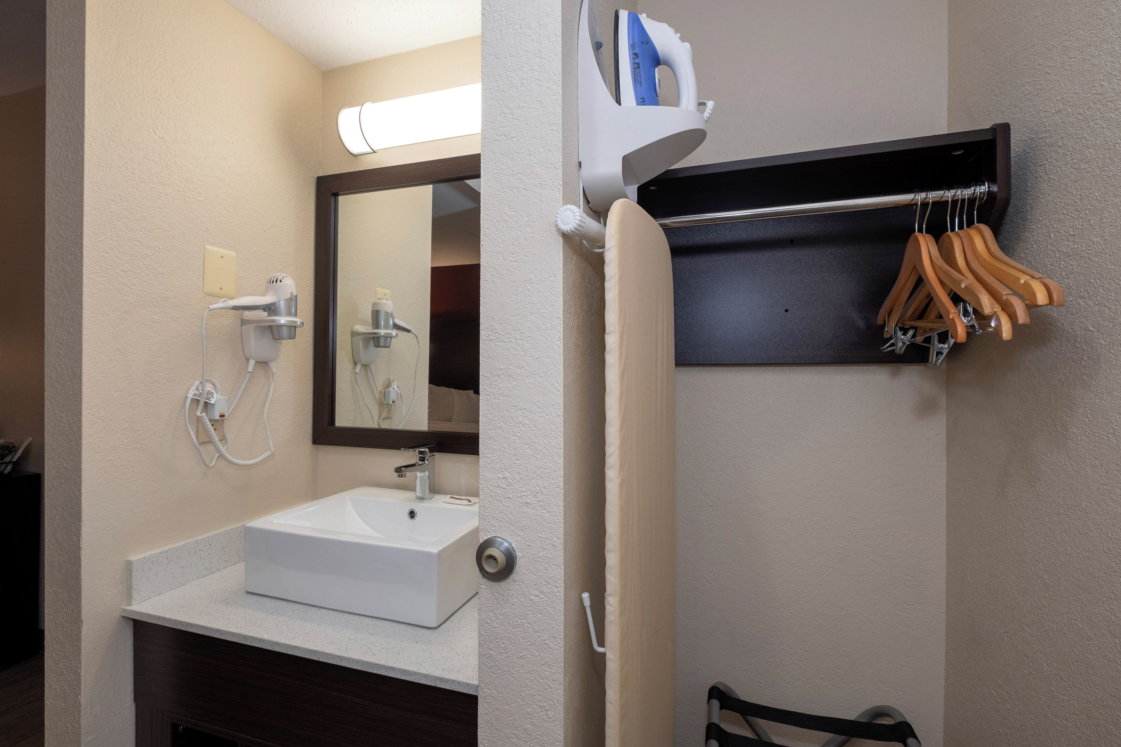 A bathroom with a white sink, a mirror, a towel rack, and a shelf with hangers.