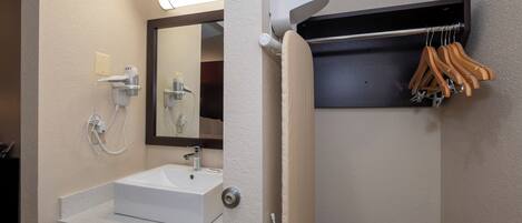 A bathroom with a white sink, a mirror, a towel rack, and a shelf with hangers.