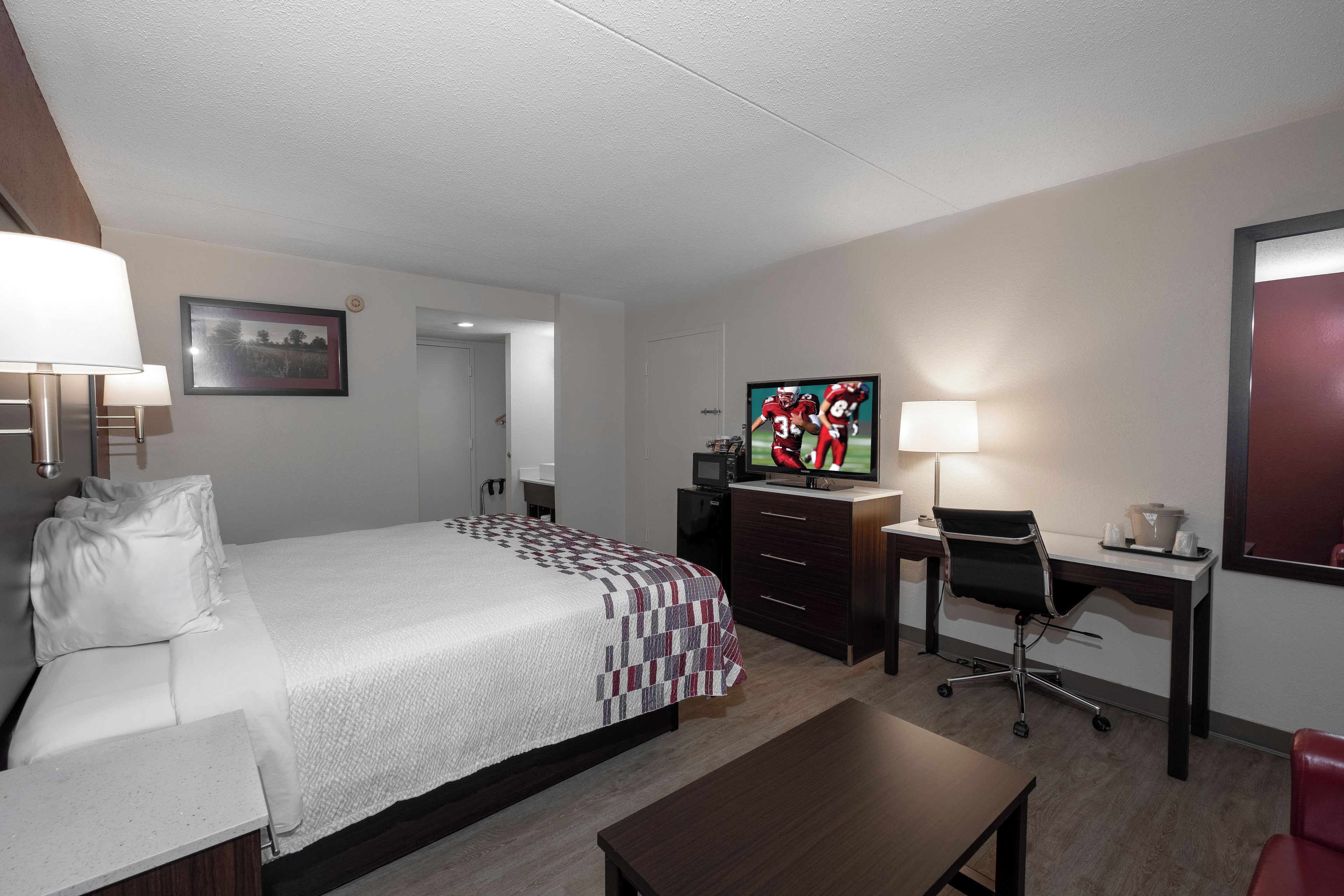 A hotel room with a bed, a desk, a chair, a television, and a lamp.