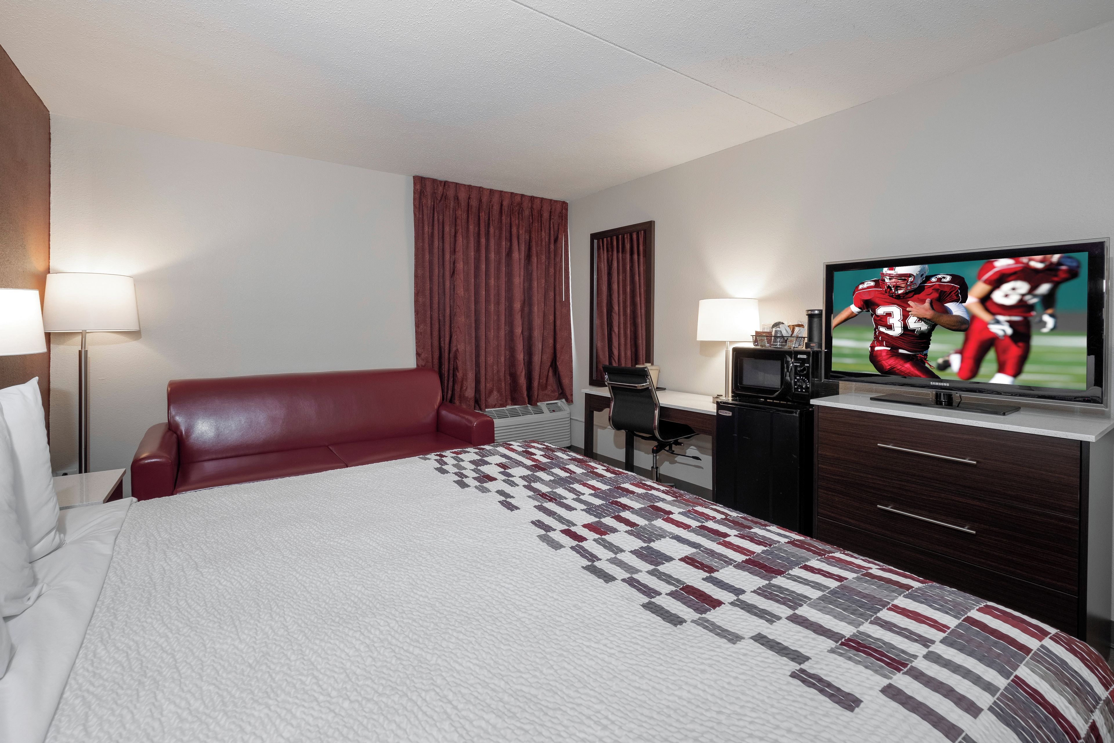 Habitación de hotel con cama, escritorio, televisión y una butaca de cuero rojo.