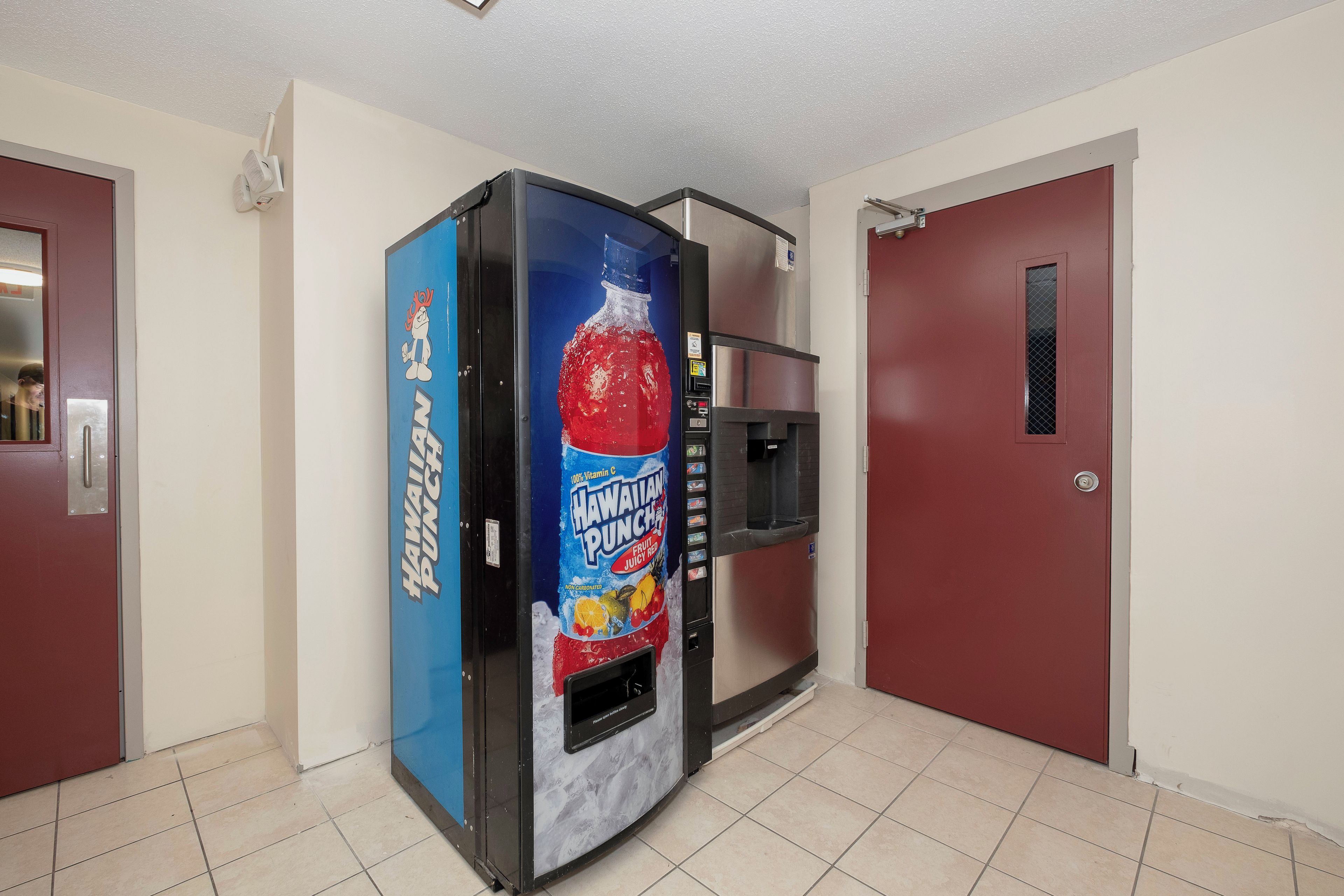 A vending machine with a Hawaiian Punch label, located in a hallway with red doors and a tiled floor.