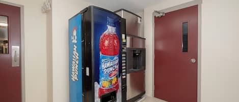 A vending machine with a Hawaiian Punch label, located in a hallway with red doors and a tiled floor.