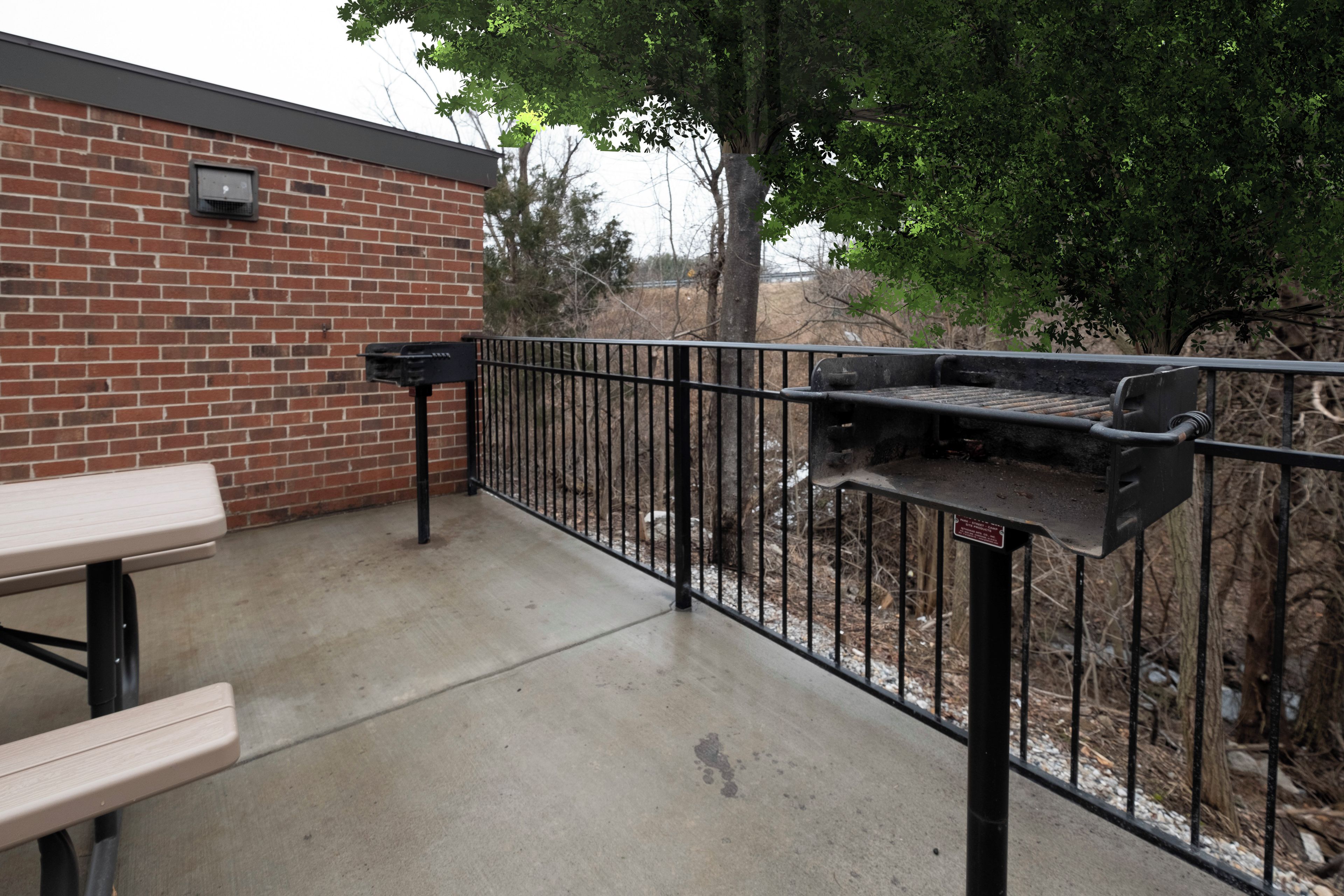 An outdoor patio area with a brick wall, a grill, and a picnic table.