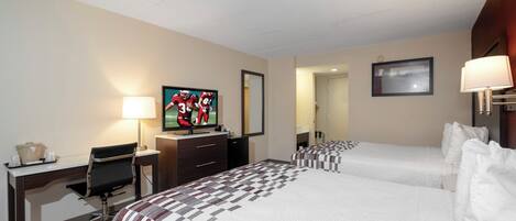 Habitación de hotel con dos camas, un escritorio con silla, televisión, lámpara y espejo.