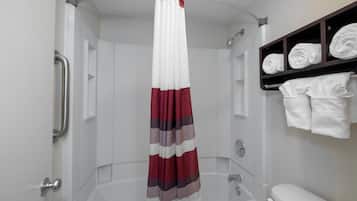 Een douche met een witte gordijn, een badkuip met glazen wand en een wit toilet.