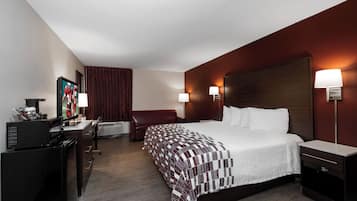 Ein Hotelzimmer mit einem Bett, Nachttischen, einem Schreibtisch mit Computer, einem Sessel und einem Fernseher.