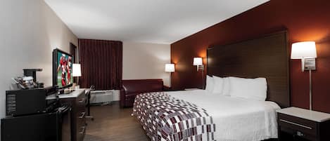 A hotel room with a bed, bedside tables, a desk with a computer, a chair, and a television.