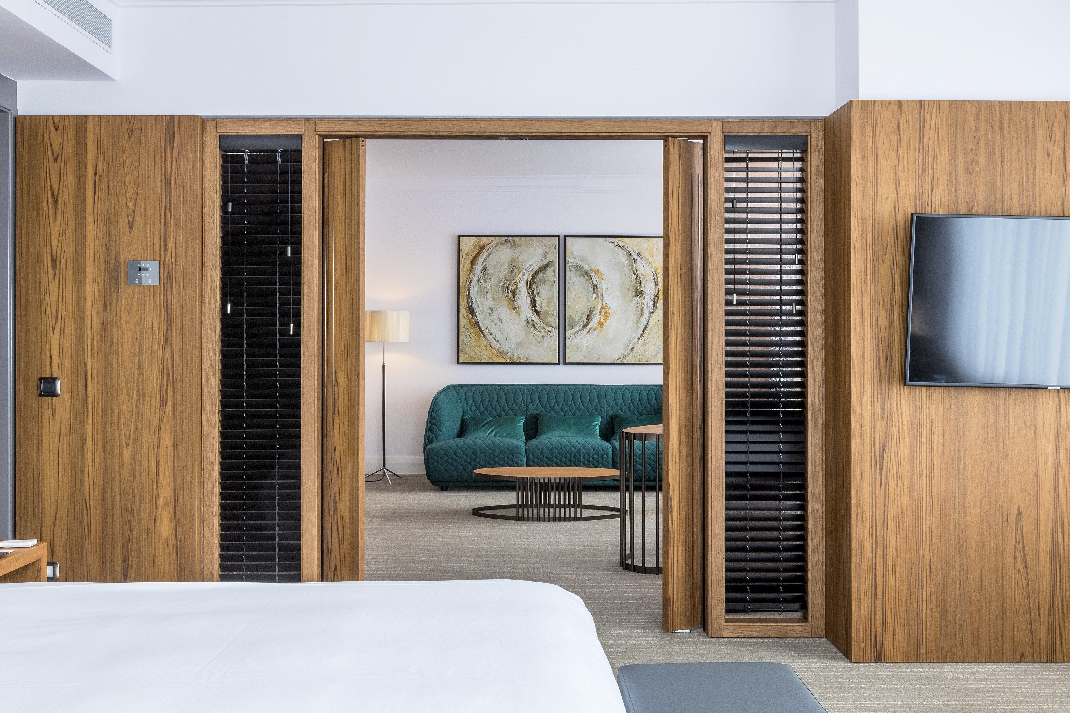 Une chambre d’hôtel moderne, dotée d’un grand lit, d’un canapé, d’une table basse et d’un téléviseur fixé au mur.