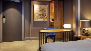 A hotel room with a bed, a desk with a chair, a lamp, and a painting on the wall.