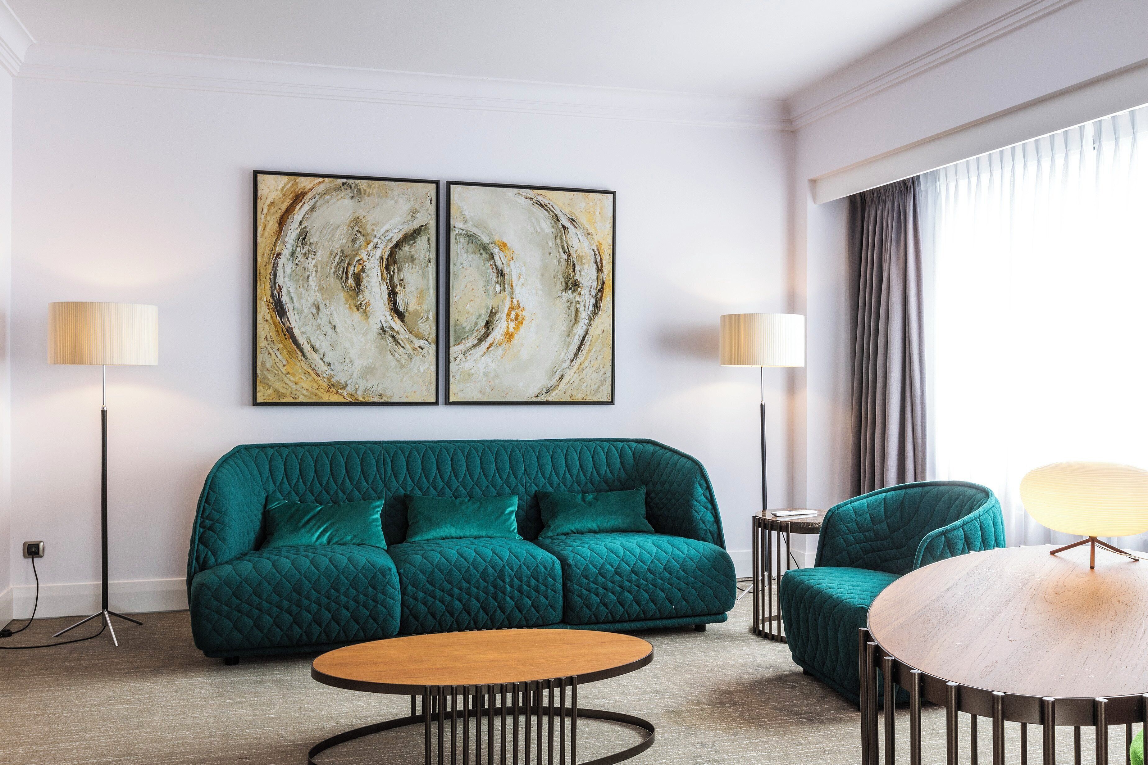 A modern living room with a teal sofa, a round wooden coffee table, and two floor lamps.