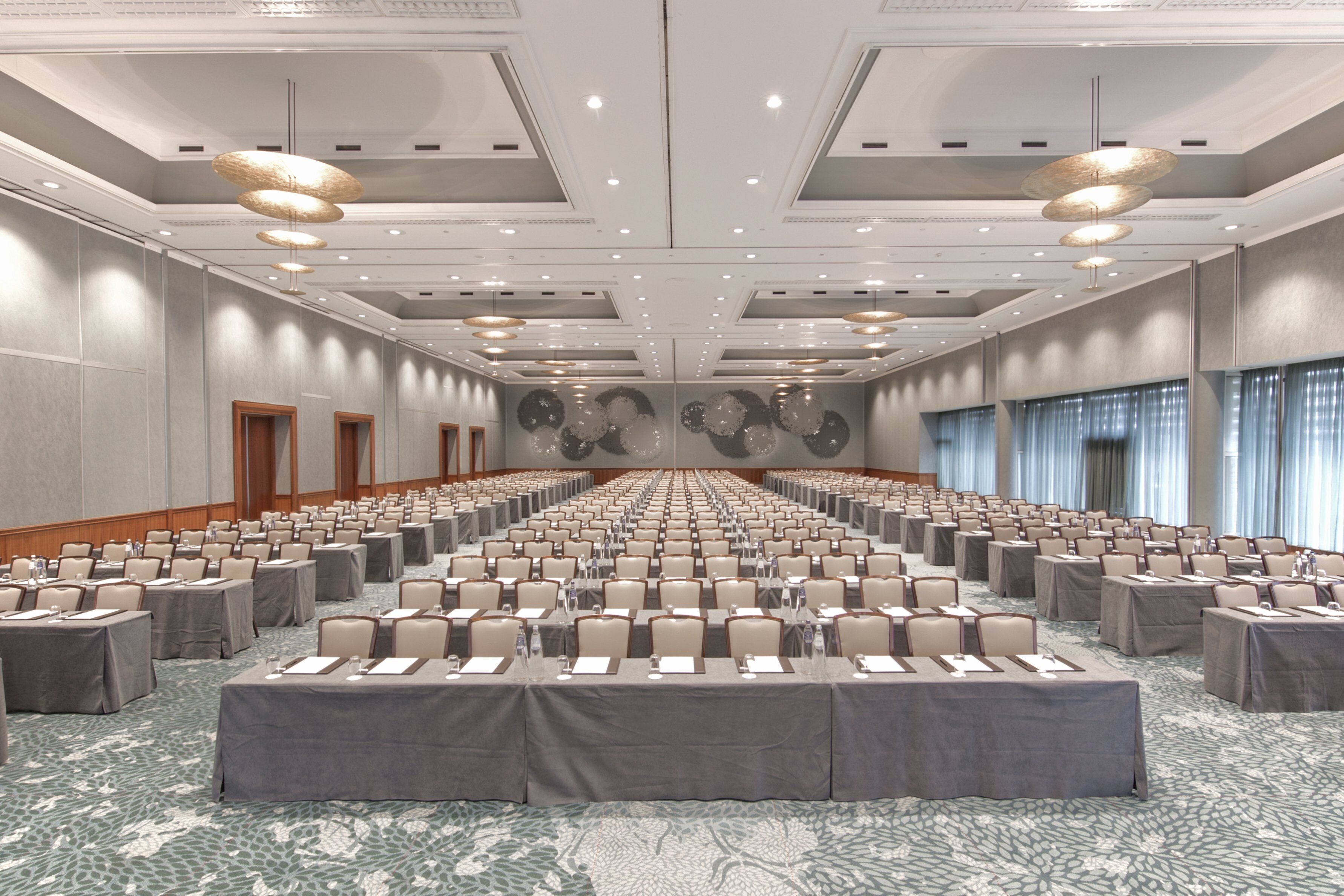 A large conference room with rows of tables and chairs, a patterned carpet, and a high ceiling with recessed lighting.