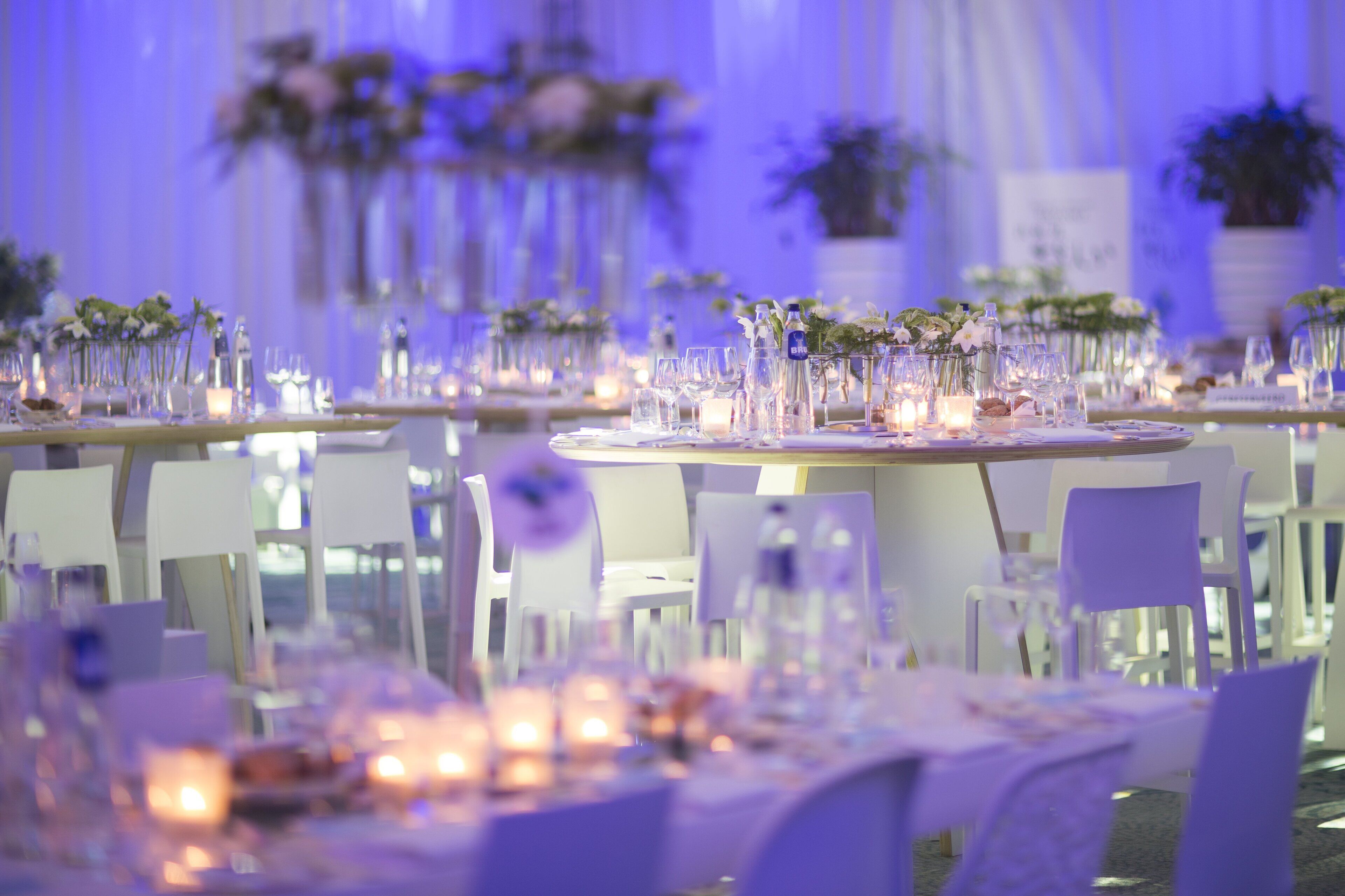 A banquet hall with round tables set for a formal event, featuring floral centerpieces and candles.