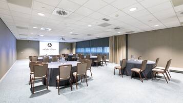 A conference room with round tables and chairs, a projector screen, and a view of the city through large windows.