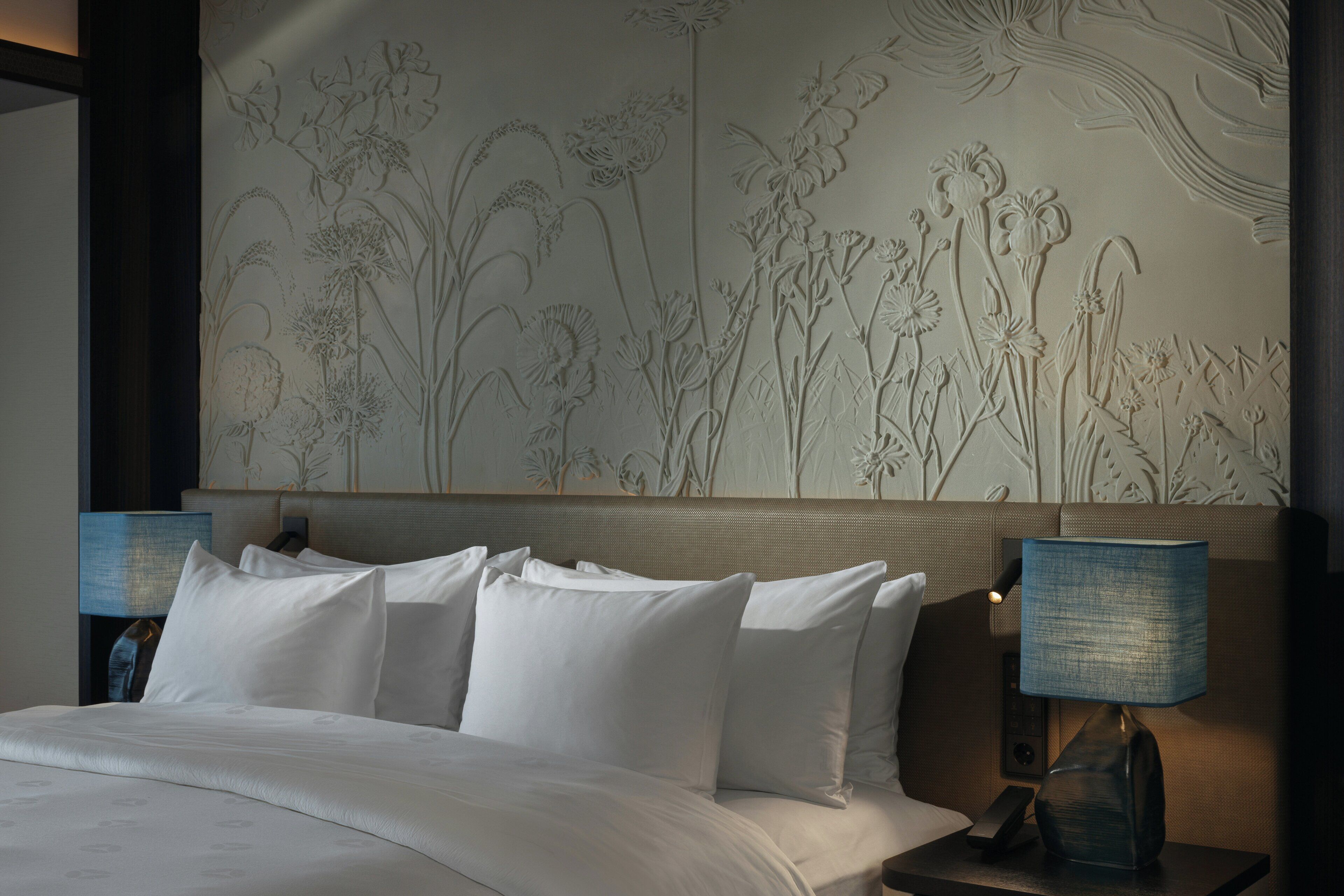 Ein Hotelzimmer mit Bett, Kissen, Kopfteil und einer Wand mit Blumenbild.