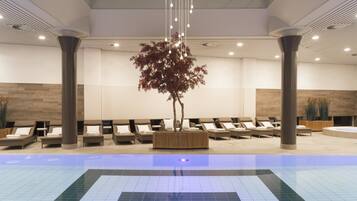 A modern indoor pool area with lounge chairs and a central decorative tree.