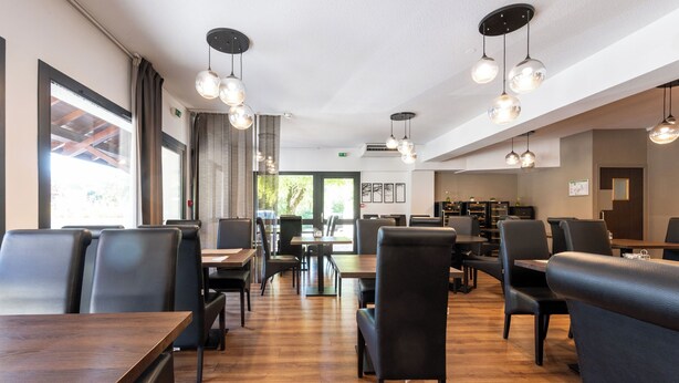 Un comedor amplio con múltiples mesas y sillas, suelo de madera e iluminación colgante.