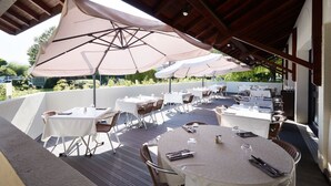 Un patio al aire libre con mesas y sillas redondas, cubierto por sombrillas grandes y una estructura de techo de madera.