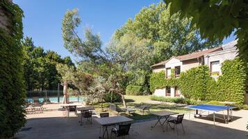 A courtyard with outdoor seating, a ping pong table, and a swimming pool in the background.