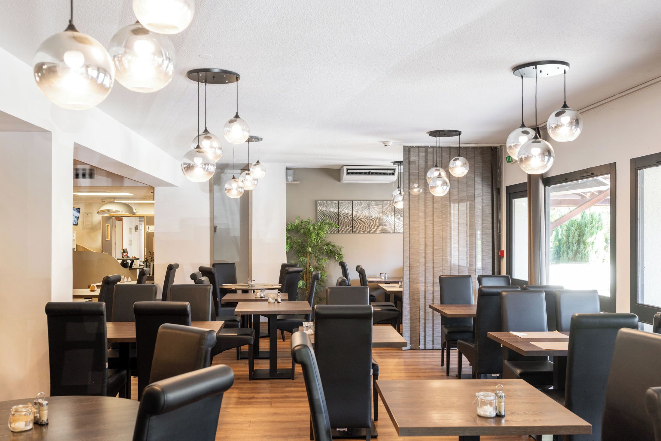 A modern restaurant interior with round tables, black chairs, and hanging spherical light fixtures.