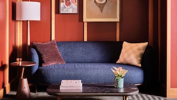 A room with a blue sofa, a wooden coffee table, a lamp, and two framed artworks on the wall.