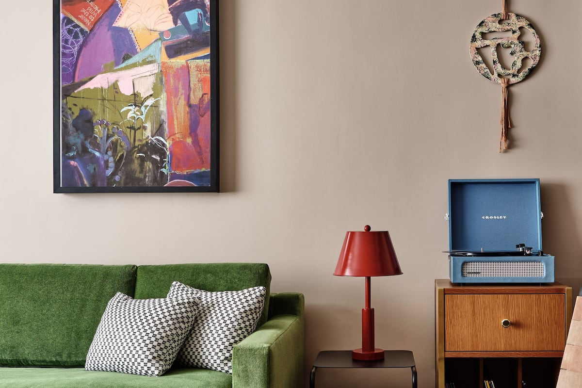 A living room with a green sofa, a red lamp, a blue record player, and a framed abstract painting.