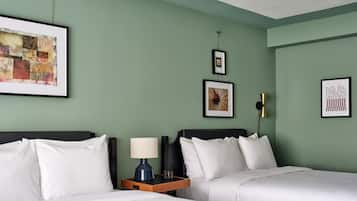 Une chambre d’hôtel avec deux lits, une table de chevet avec une lampe et trois œuvres d’art encadrées accrochées au mur.