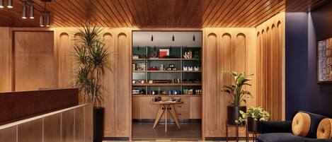 Un espace d’accueil moderne avec un plafond en bois, un comptoir d’accueil, un coin salon avec un canapé et une bibliothèque remplie de divers objets.