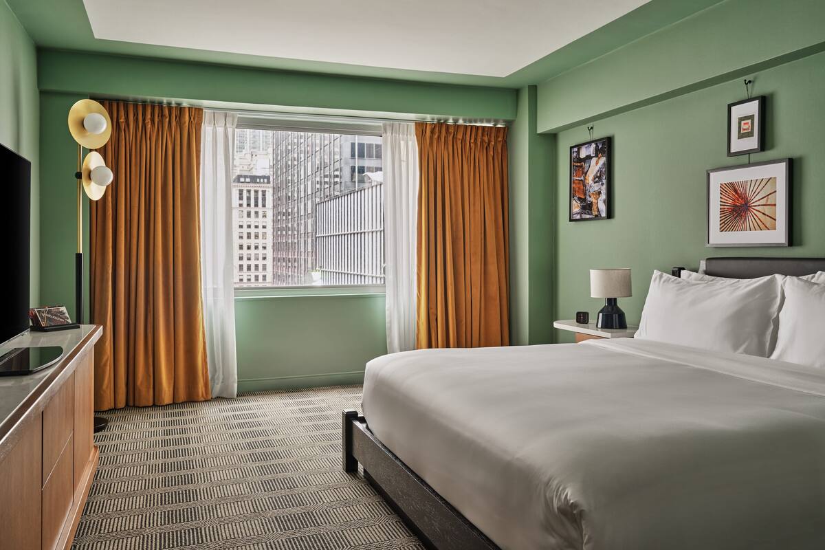 A hotel room with a large bed, a desk with a lamp, a television, and a window with curtains.