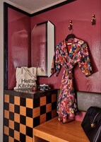 A room with a checkered wooden desk, a robe hanging on the wall, a camera, and a 'Hell's Kitchen' bag.
