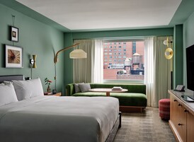 Een hotelkamer met een groot bed, een groene bank, een kleine tafel, een televisie en uitzicht op de stad.