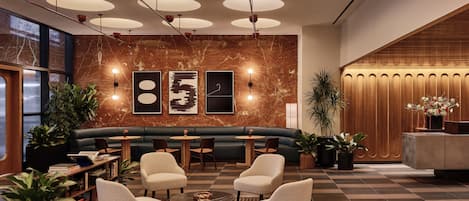 Um lobby moderno com um sofá verde, duas poltronas e uma mesa de centro. Há plantas em vasos e uma mesa de recepção com acabamento em madeira.