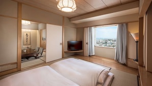 A hotel room with a large bed, a television, a dining table with chairs, a view of the city, and traditional Japanese decor. - DoubleTree by Hilton Naha Shuri Castle (Naha)