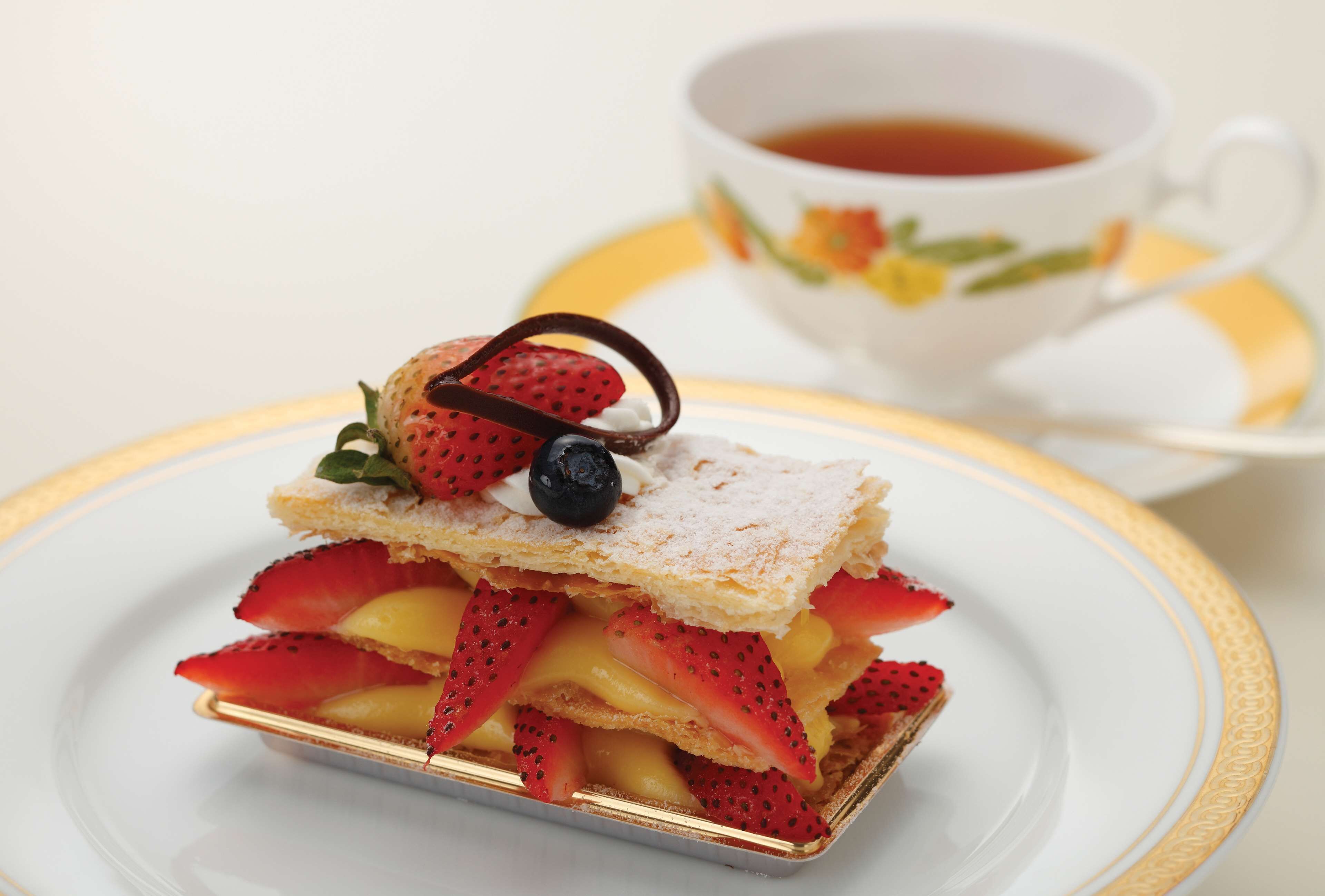 A dessert with strawberries and a chocolate piece on a white plate with a gold rim.