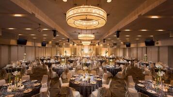 A banquet hall with round tables, white chairs, and chandeliers.