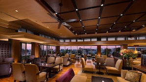 A spacious lounge area with multiple seating options, including sofas and chairs, arranged around a central coffee table. Large windows provide views of the cityscape. - DoubleTree by Hilton Naha Shuri Castle (Naha)