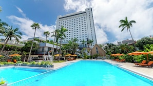 A hotel pool with a clear blue pool, surrounded by palm trees and orange umbrellas. - DoubleTree by Hilton Naha Shuri Castle (Naha)