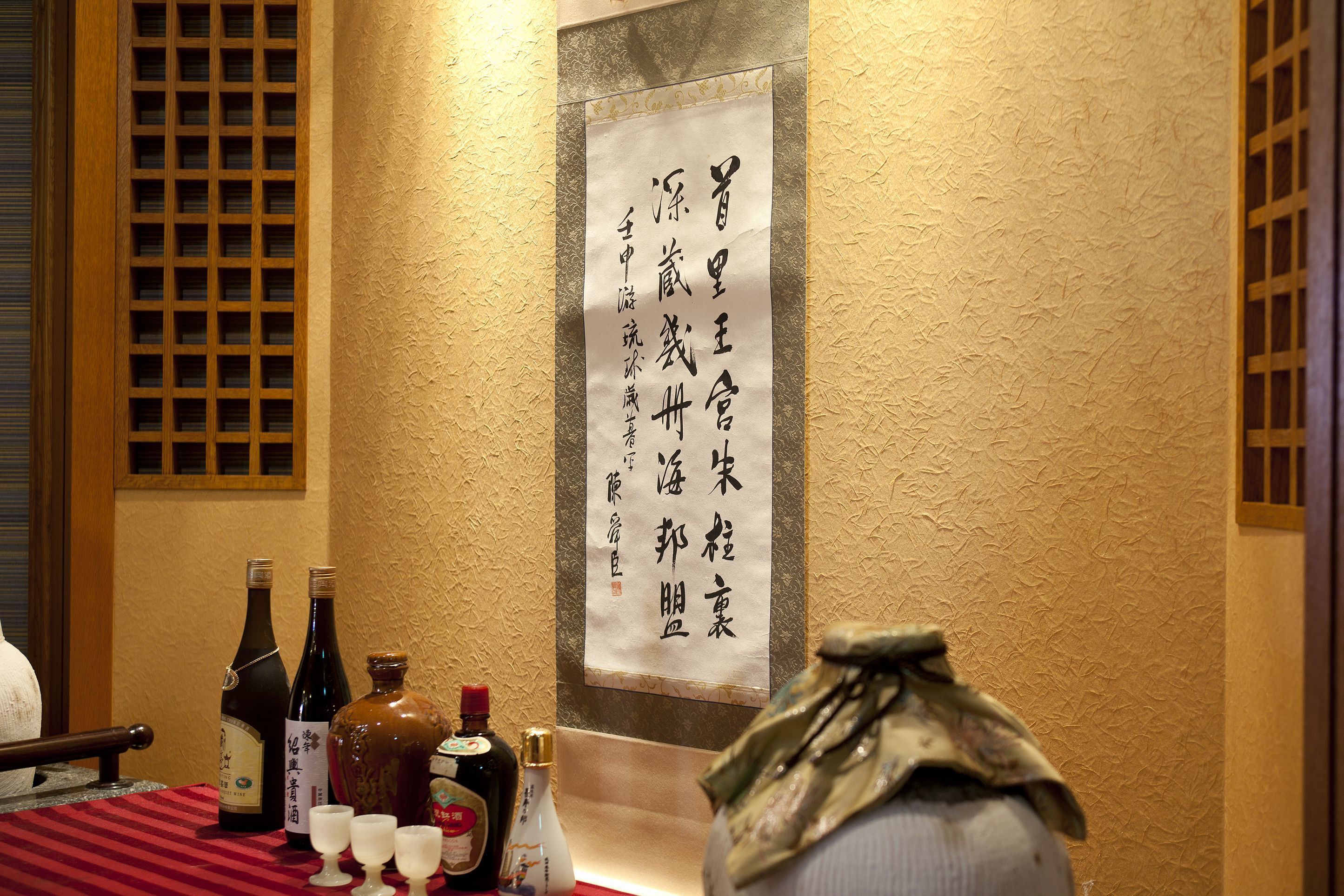 A table with bottles and glasses, a decorative wall with a hanging sign, and a traditional wooden lattice window.