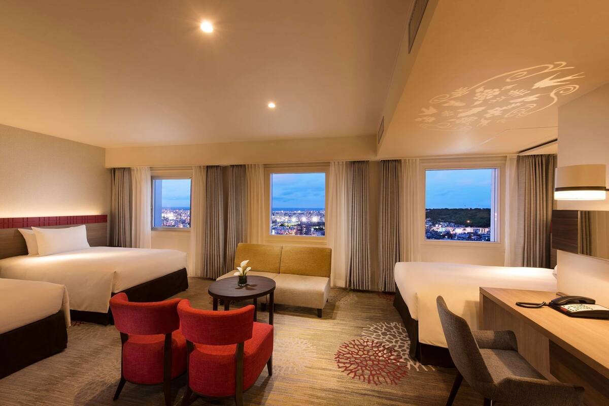 A hotel room with two beds, a sofa, a small table, and a desk with a phone.