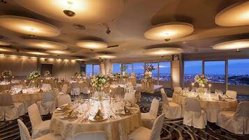 A banquet hall with round tables set for a formal event, large windows with a city view, and a modern ceiling design.