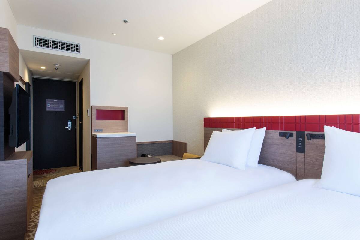 A hotel room with a large bed, a desk, a chair, and a red accent wall.