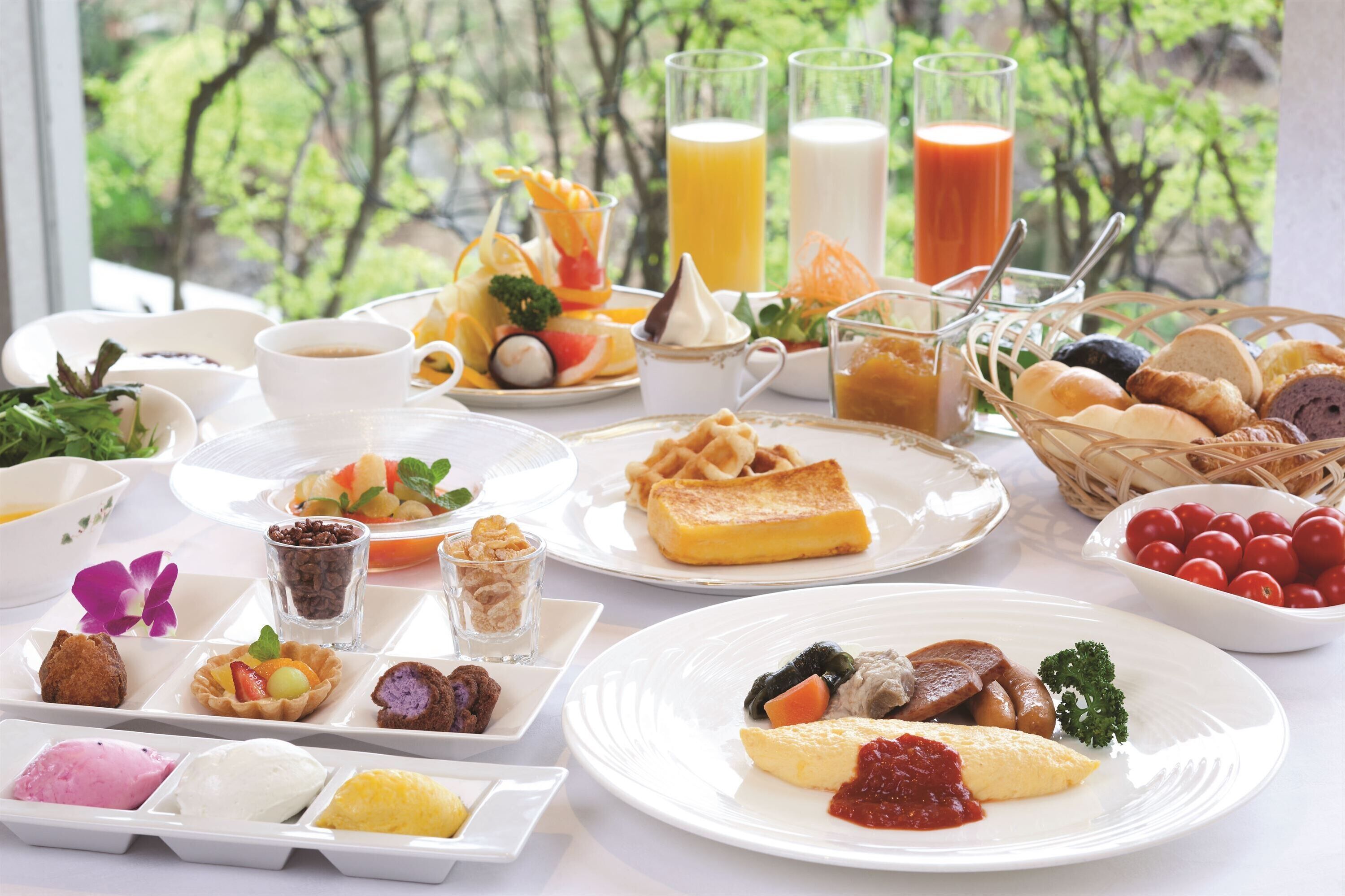 Une table dressée avec divers aliments pour le petit-déjeuner, notamment des gaufres, des œufs et des viennoiseries, et en arrière-plan, une vue sur des arbres.