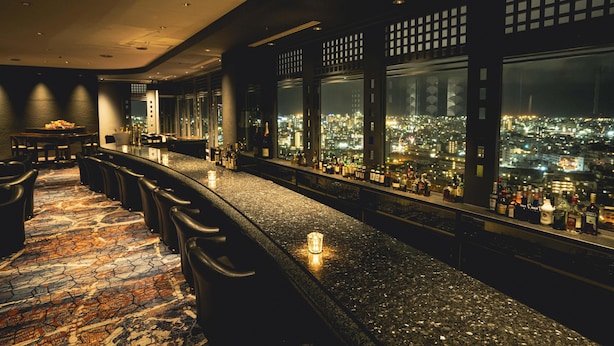 A bar with a city view, bar stools, and bottles. - DoubleTree by Hilton Naha Shuri Castle (Naha)